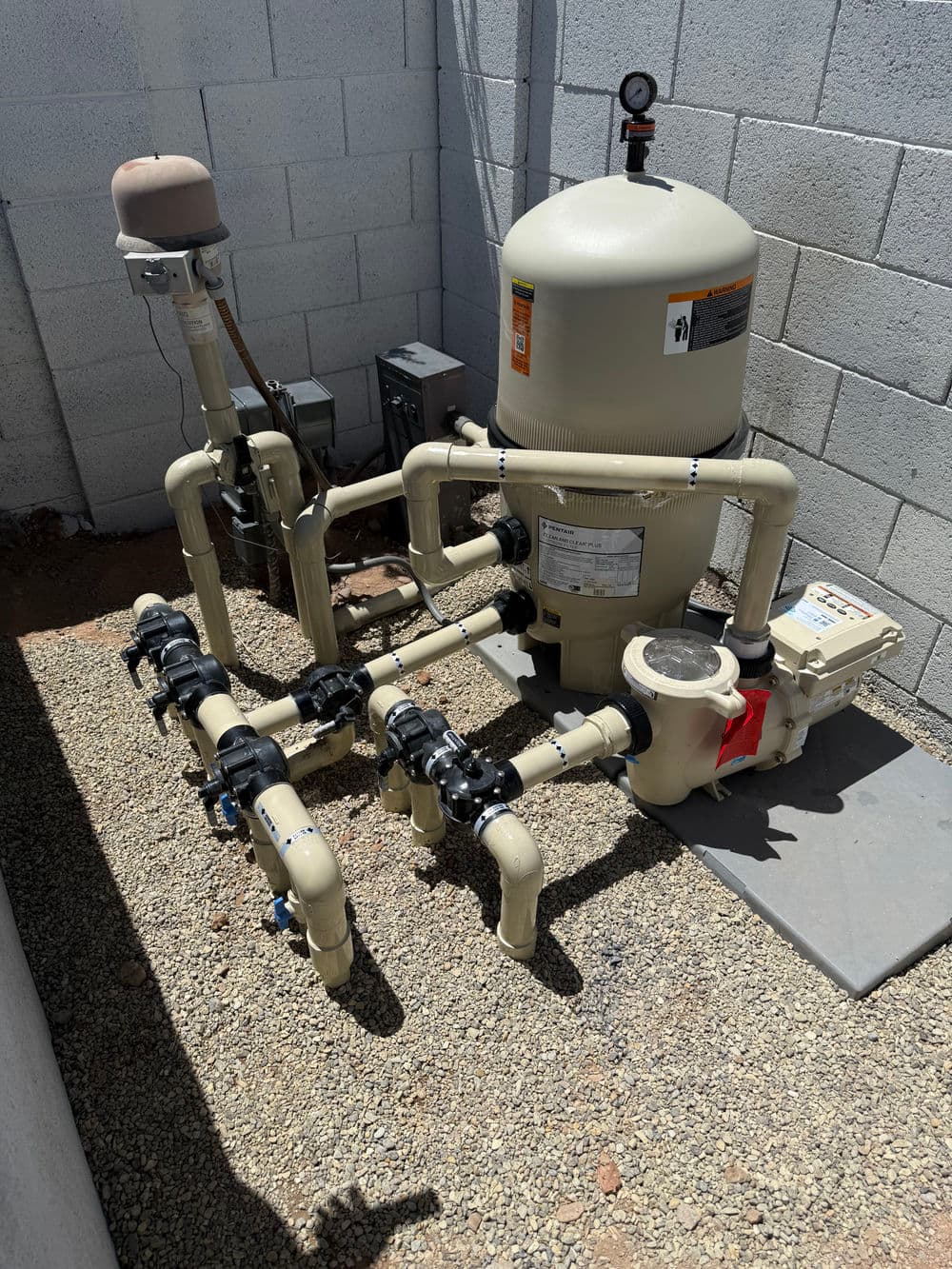 Pool filtration system with pipes and pump, located against a concrete wall.