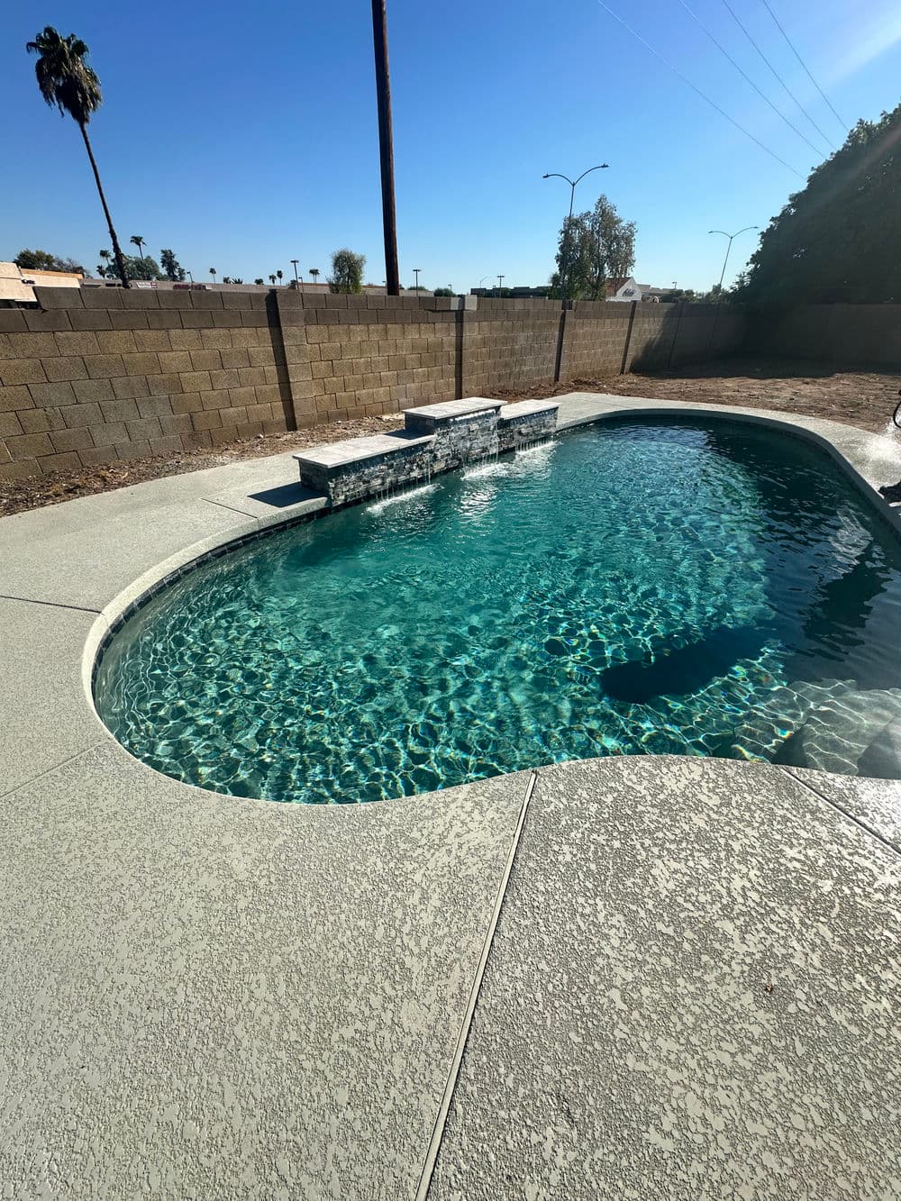 Crystal clear swimming pool with waterfall feature and palm trees in the background.