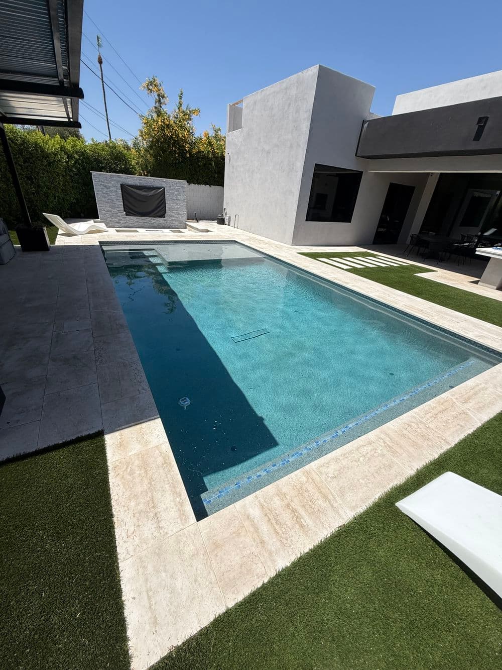 Modern backyard pool surrounded by stylish patio, grass, and a sleek house design.