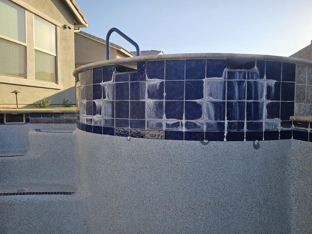 Round hot tub with blue tiles, showing signs of water damage, against a house exterior.