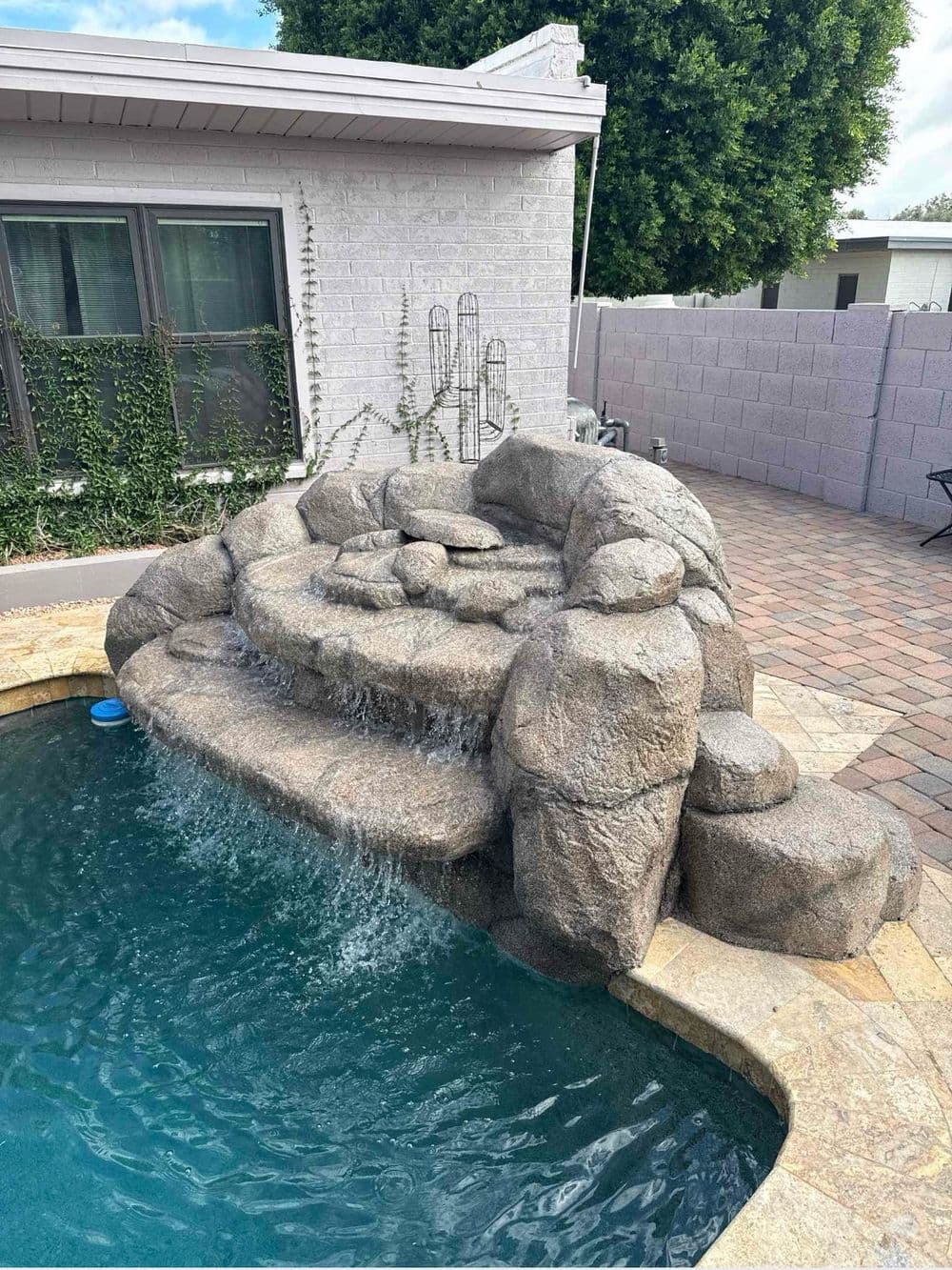 Rock waterfall feature cascading into a swimming pool, enhancing backyard landscape.