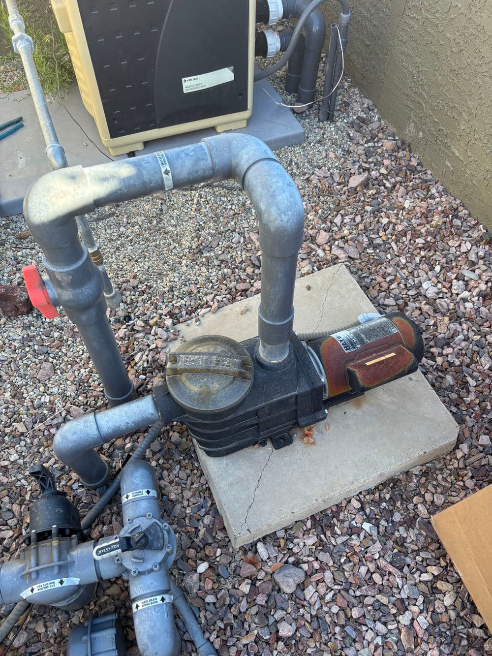 Submersible water pump on concrete slab with surrounding pipes and gravel base.