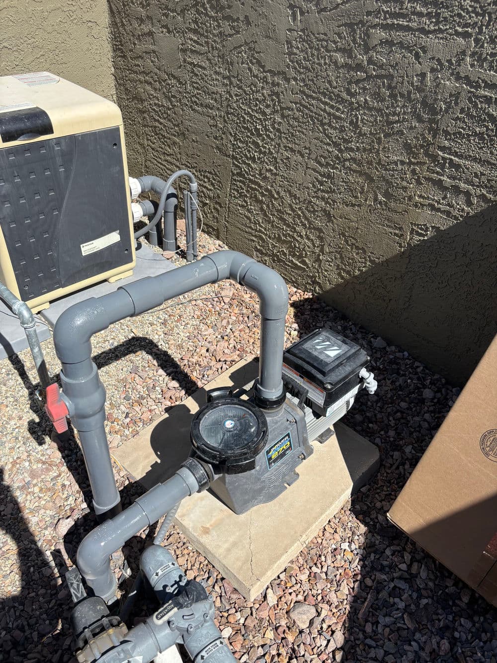 Pool pump system with gray pipes and control box against a textured wall.