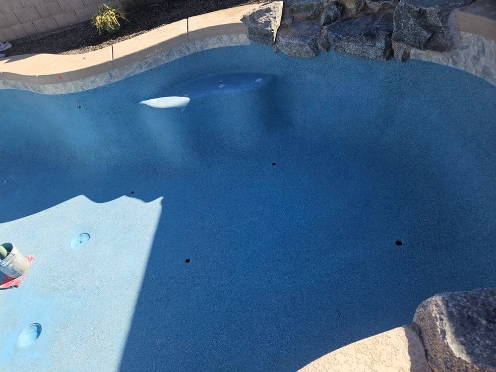 Empty swimming pool with a textured blue surface and surrounding stone details.