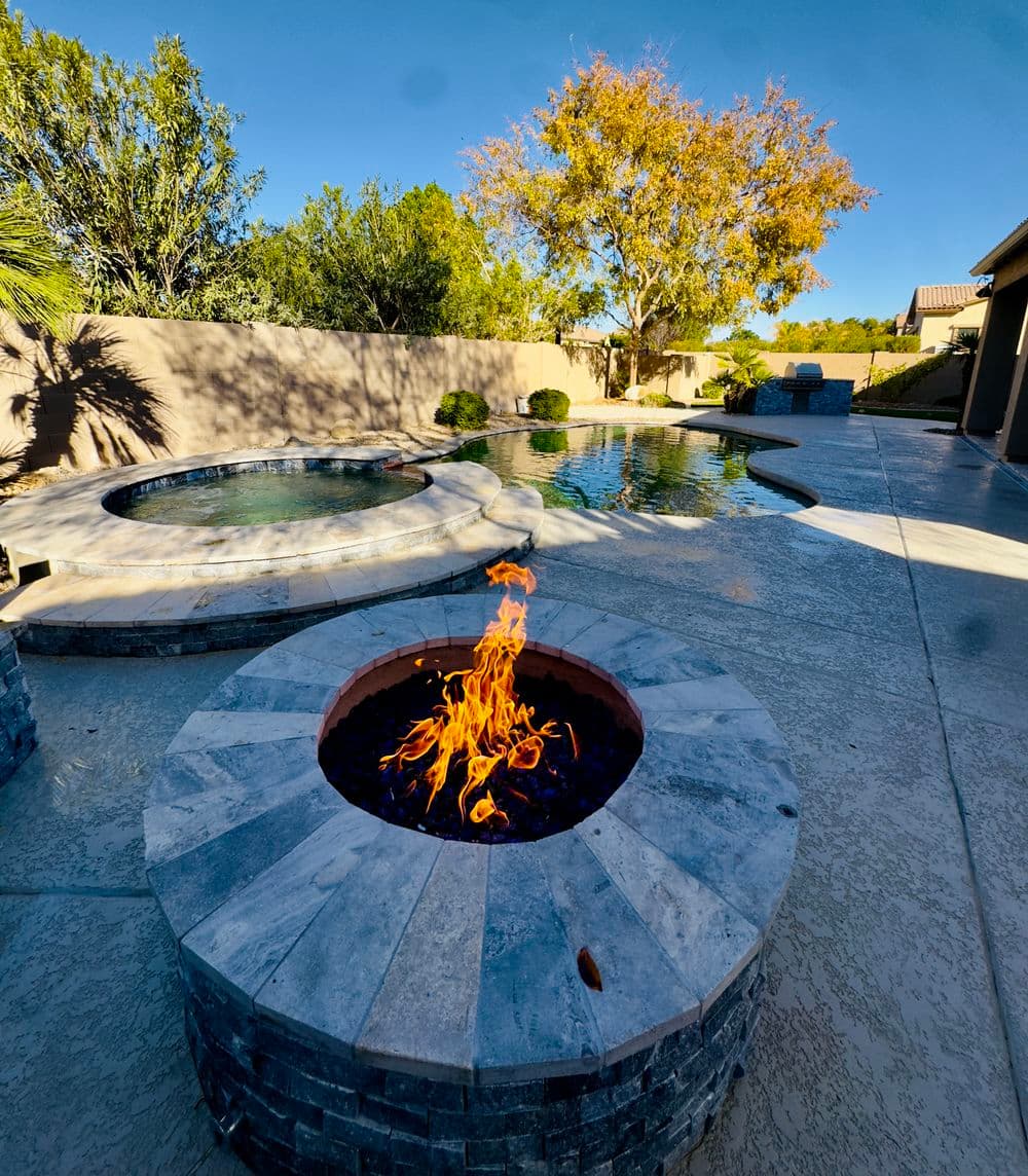 Modern backyard with a fire pit, swimming pool, and spa surrounded by lush greenery.