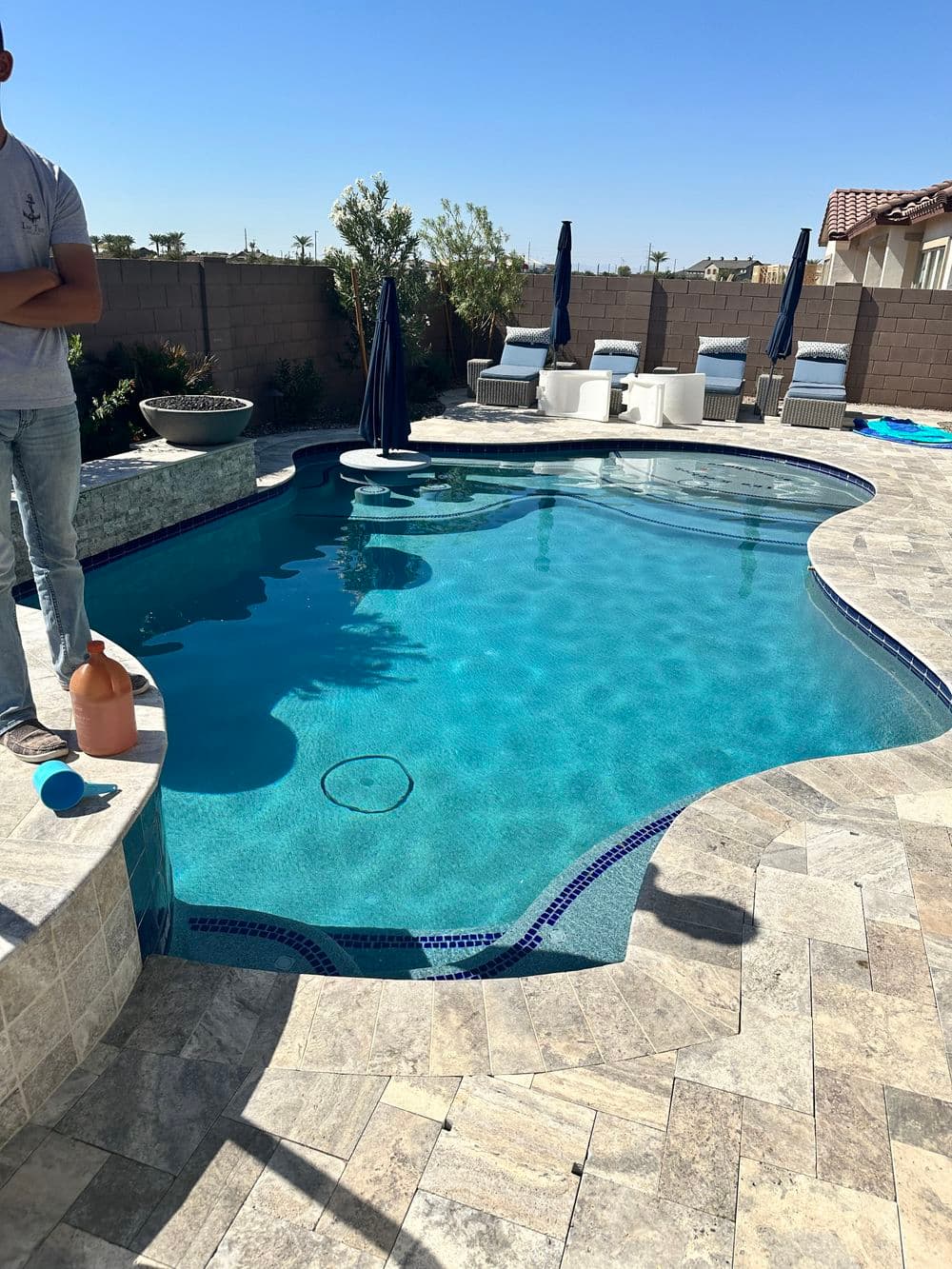 Backyard pool with clear water, stone deck, lounge chairs, and sunlight on a clear day.