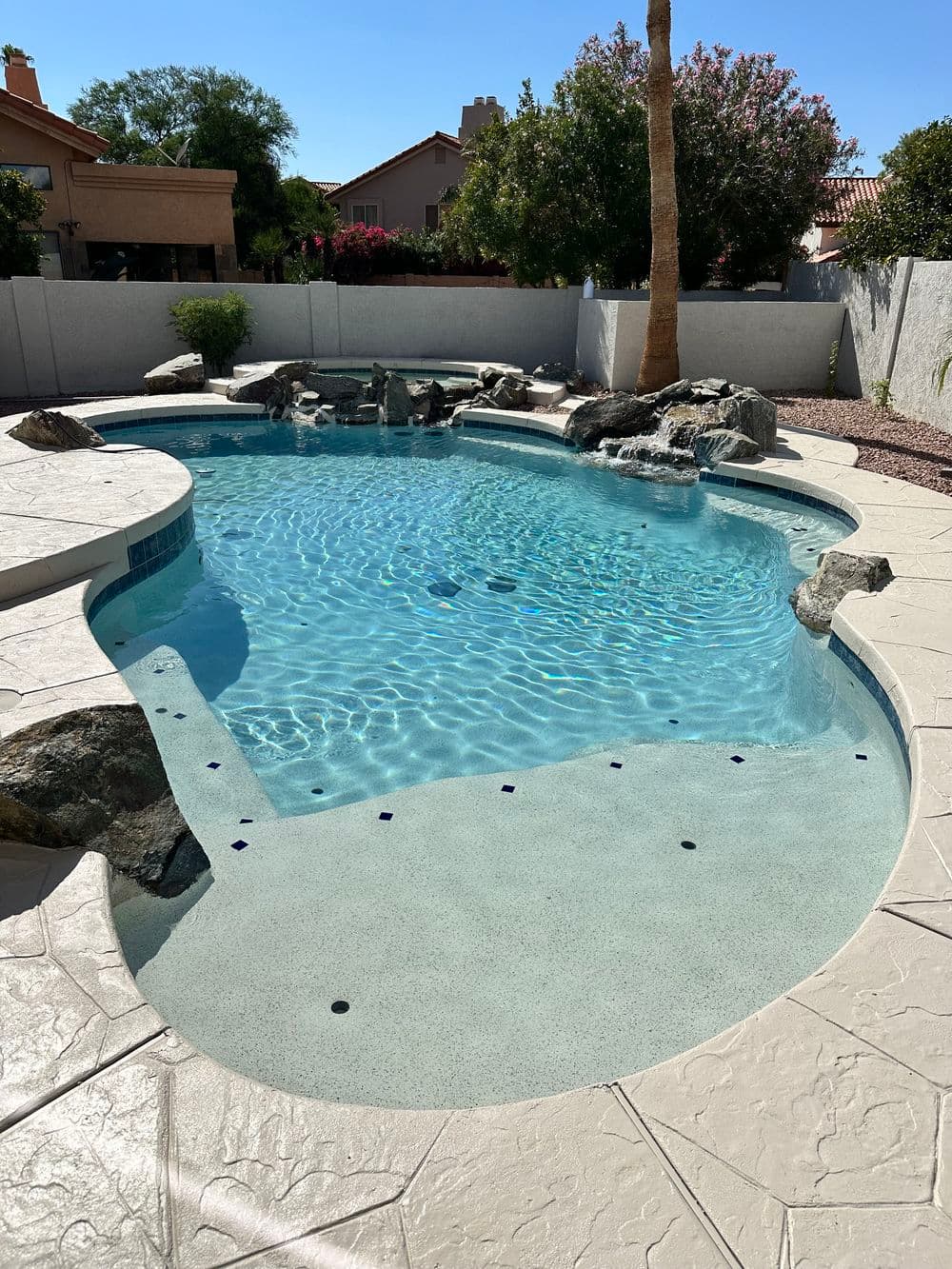 Sparkling swimming pool with rock formations and surrounding landscaping in a sunny backyard.