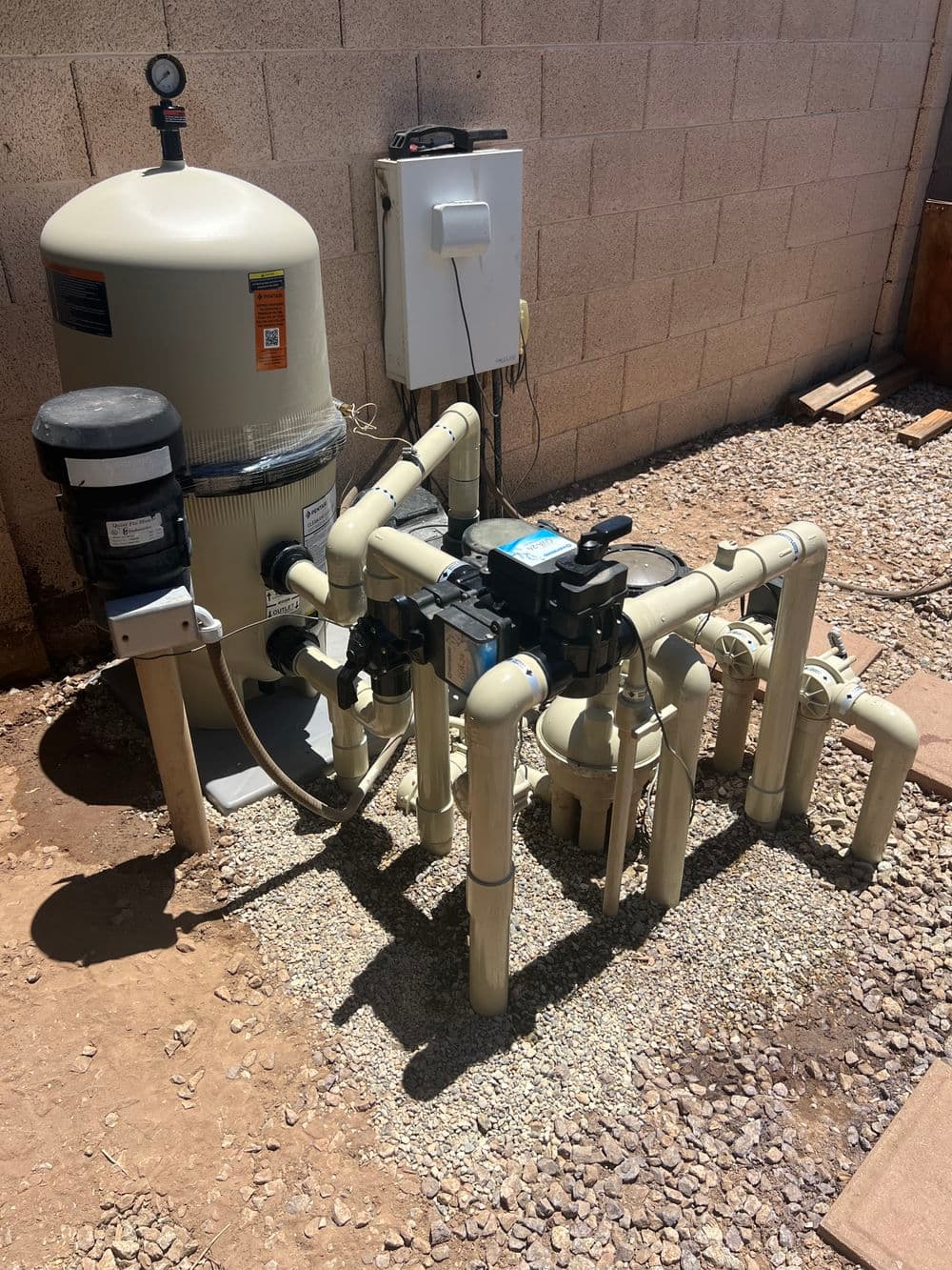 Swimming pool equipment setup with pump, filtration system, and PVC plumbing in a backyard.