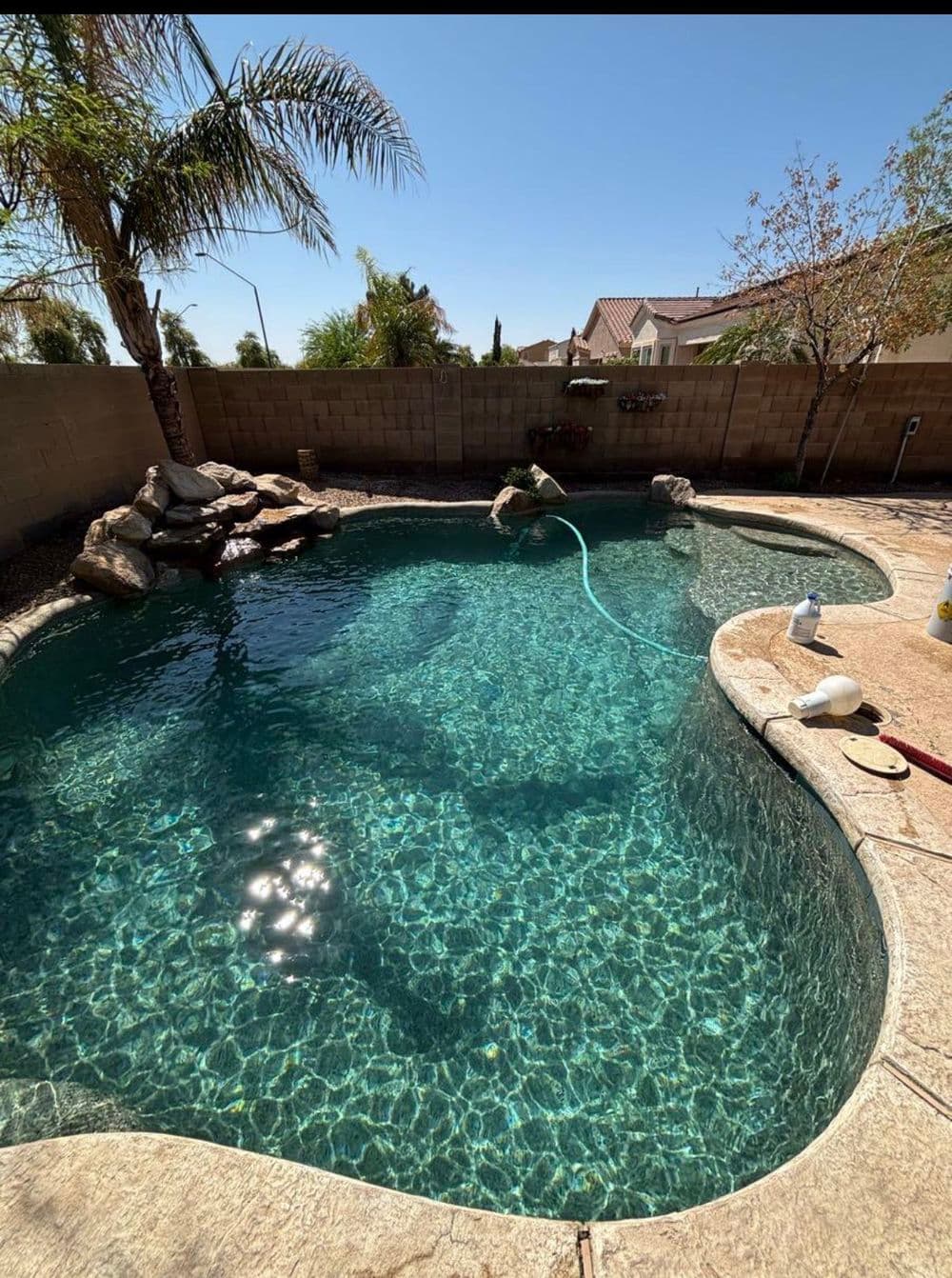 Sparkling blue swimming pool surrounded by palm trees and stone features on a sunny day.